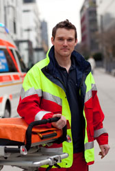 Foto: Sanitäter steht mit einer Trage vor einem DRK-Wagen.